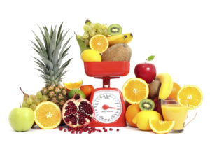 Food scale loaded with and surrounded by colorful fruits.