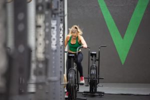 Female athlete alone on the Assault Bike in the back of the gym.