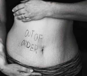 Woman holding bare stomach with "out of order" written on it in ink.