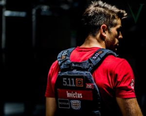 Male athlete wearing a CrossFit weight vest staring into the darkness of the gym.