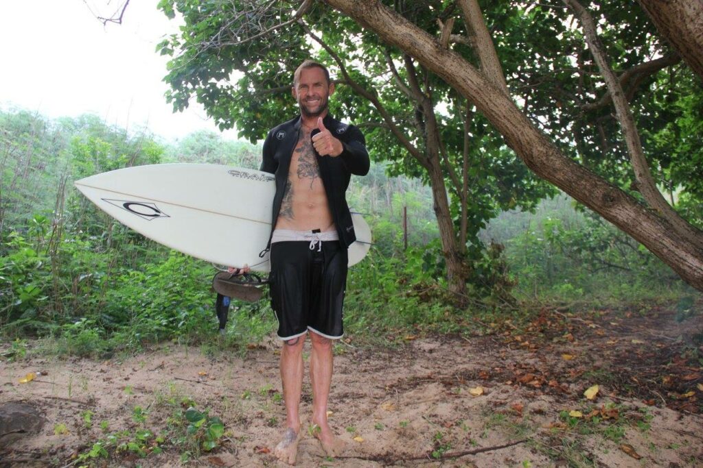 Brandon Lillard standing on a trail to the beach with his short board.