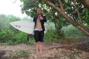 Brandon Lillard standing on a trail to the beach with his short board.