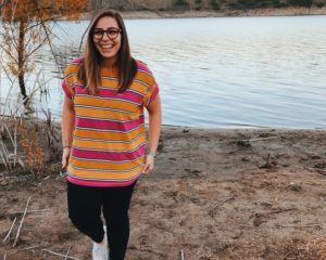 Female in a bright striped shirt smiling in front of a lake.