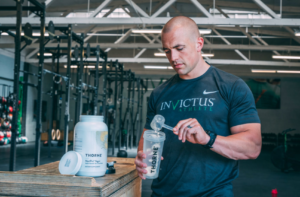 Invictus athlete putting protein powder into his shaker bottle.