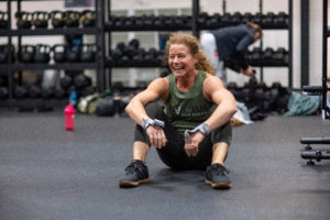 Female masters athlete sits on the ground laughing with her arms on her legs.