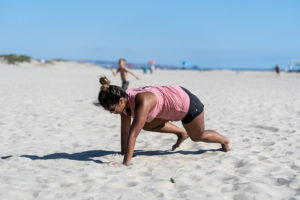 Female athlete doing a bear crawl in the sand at the beach.