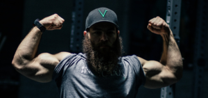 Bearded male athlete coming out of the shadows while flexing his biceps.