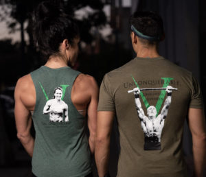 A male and a female athlete wearing "Invictus Masters" shirt and tank facing away from the camera.