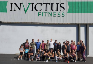 Large group of athletes posing after a great workout under the Invictus sign.