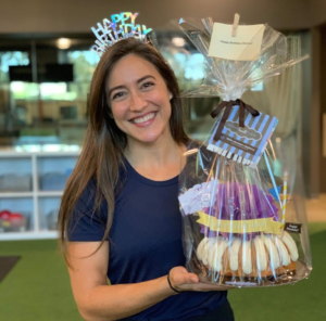 Smiling woman wearing a happy birthday Tiera and holding a gift wrapped bundt cake.