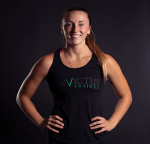 Female athlete poses with her hands on hips while wearing a stylish black Invictus tank top.