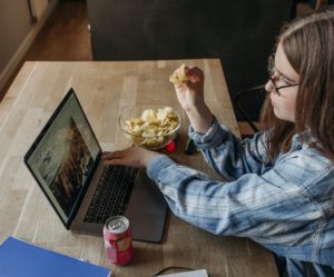 A woman eating while working on her laptop.
