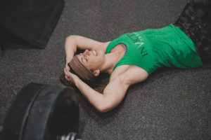 Female athlete laying on the floor with her hands above her head trying to catch her breath after a grueling workout.