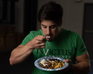 Male wearing an Invictus shirt while eating a heaping plate of food.