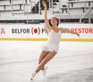 Female figure skater on the ice making a turn with her arm in the air.