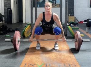 Female Invictus weightlifter wearing singlet in the set-up position for a clean on the platform.