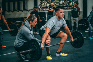 A coach works with an athlete on pulling their knees back on the snatch liftoff.
