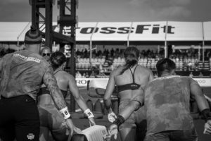 Team Invictus, backs to camera and hands on pillar, at the starting line of one of the 2022 CrossFit Games workouts.