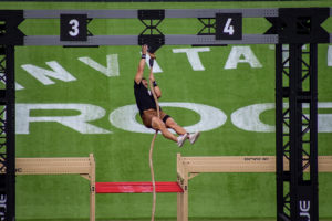 Male athlete at the top of a rope climb in a competition.