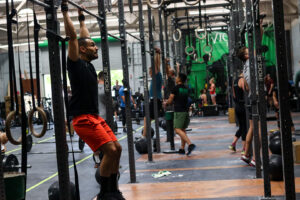 Male athlete hanging from pull-up bar in group training session.