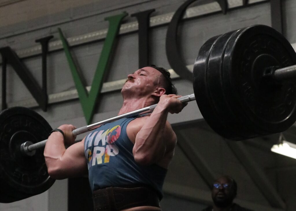 Invictus Weightlifter with a massively heavy barbell in the front rack position getting ready to go overhead.