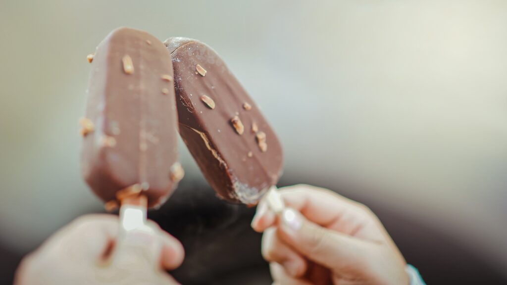 Two people doing a "cheers" with ice cream bars.