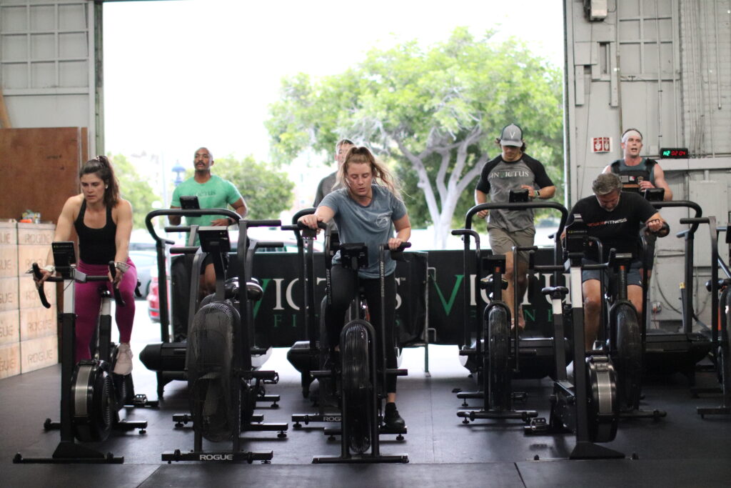 Invictus group coaching members using the Assault Runners and Bikes with the open gym door in the background.