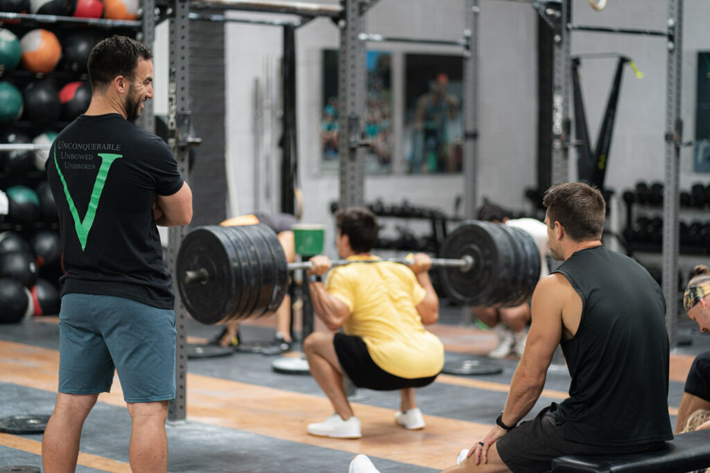 Athlete performing a heavy back squat with his coach and teammate watching.